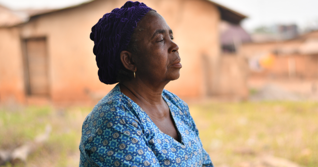 An old black woman in a rural setting with her eyes closed